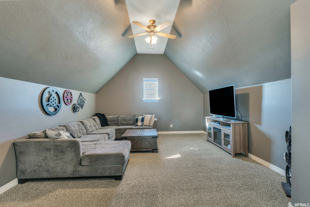 Carpeted living room featuring lofted ceiling, ceiling fan, and a textured ceiling