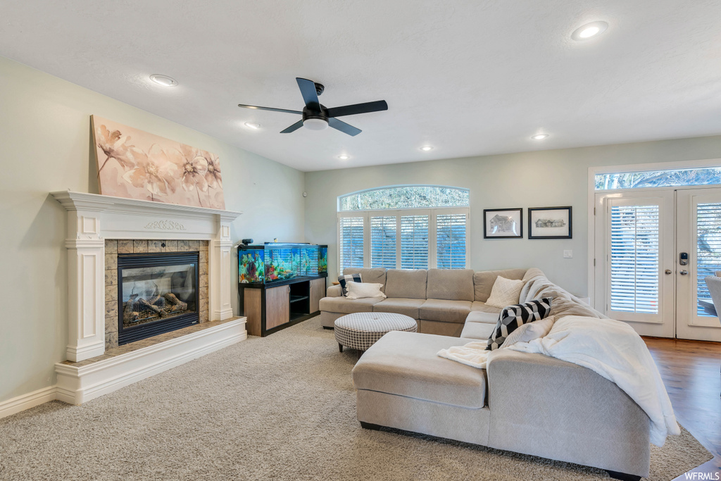 Living room featuring light colored carpet, ceiling fan, a fireplace, and plenty of natural light