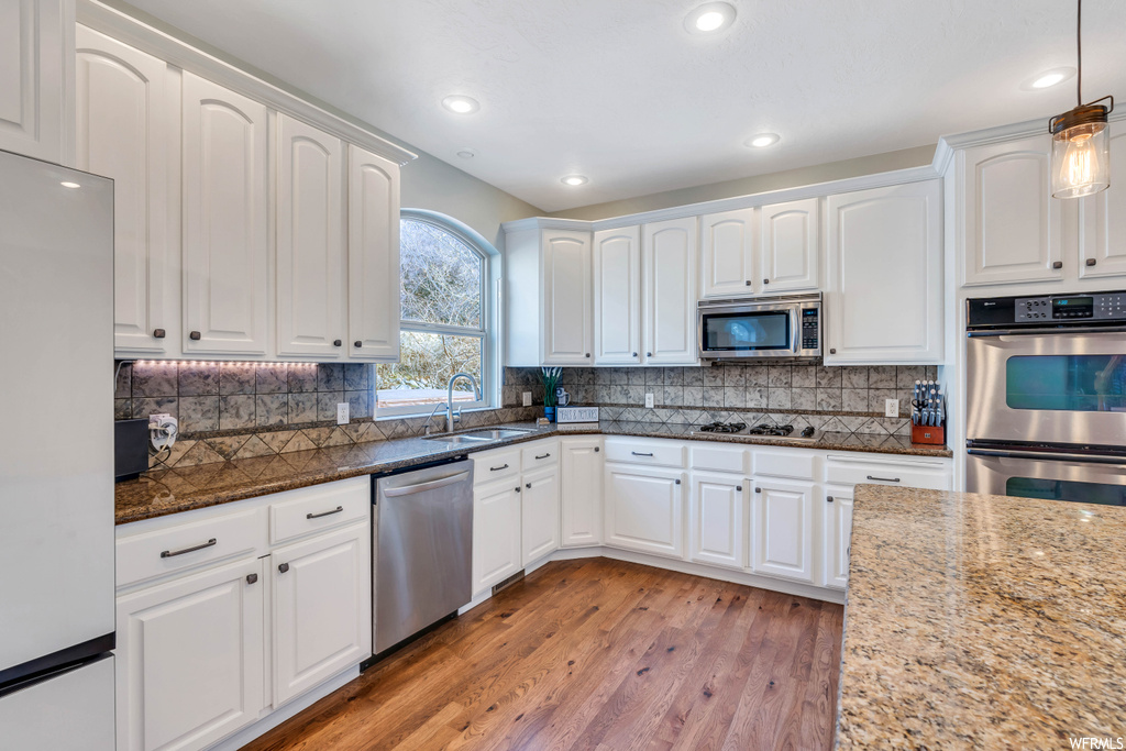 Kitchen with pendant lighting, white cabinets, stainless steel appliances, and light hardwood / wood-style floors