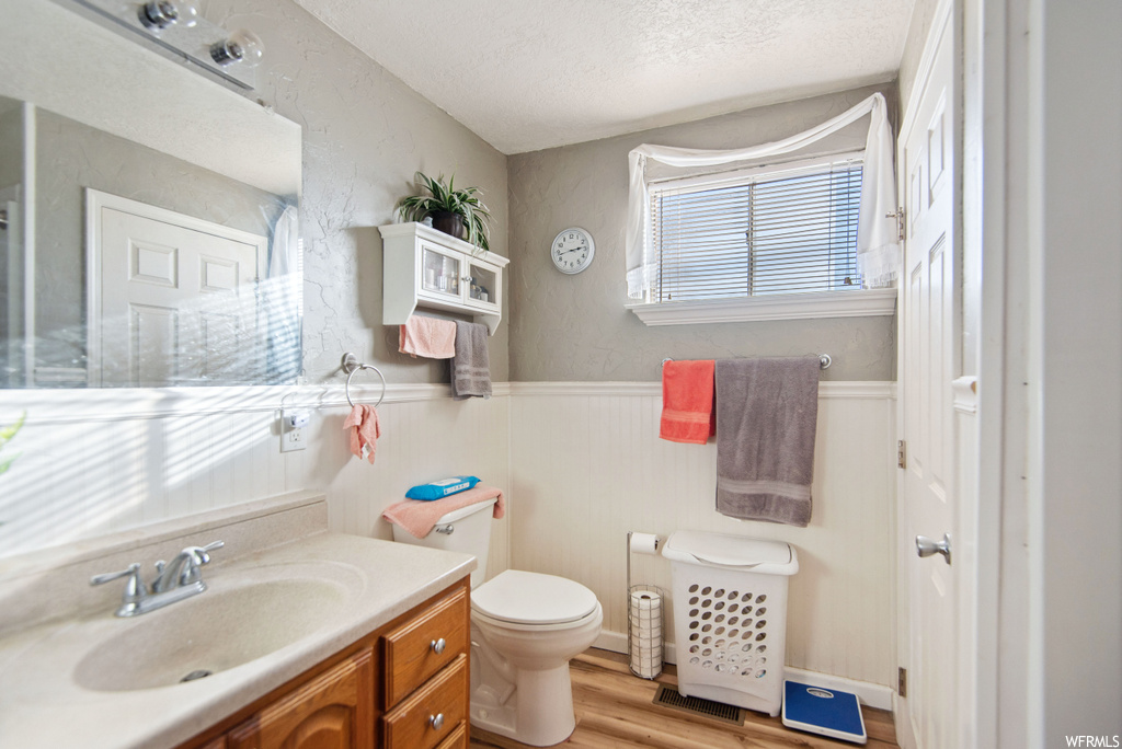 Bathroom featuring toilet, vanity with extensive cabinet space, a textured ceiling, and hardwood / wood-style floors