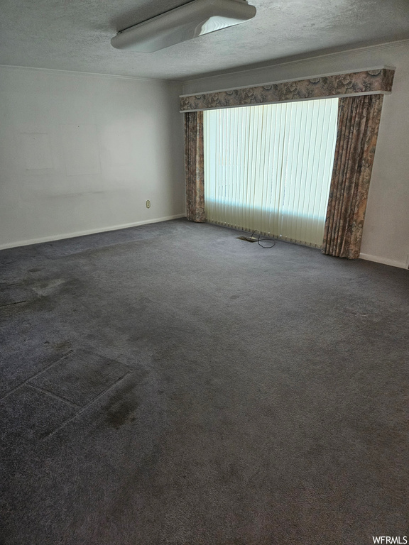 Empty room with dark carpet and a textured ceiling