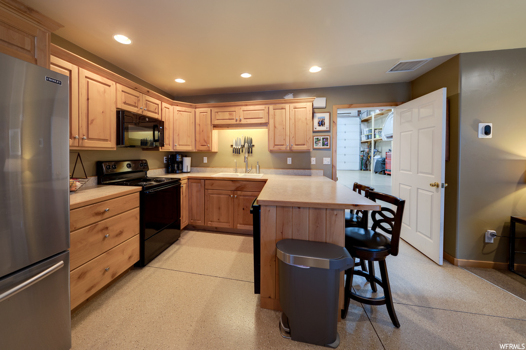 Kitchen featuring sink, black appliances, light brown cabinets, and a breakfast bar