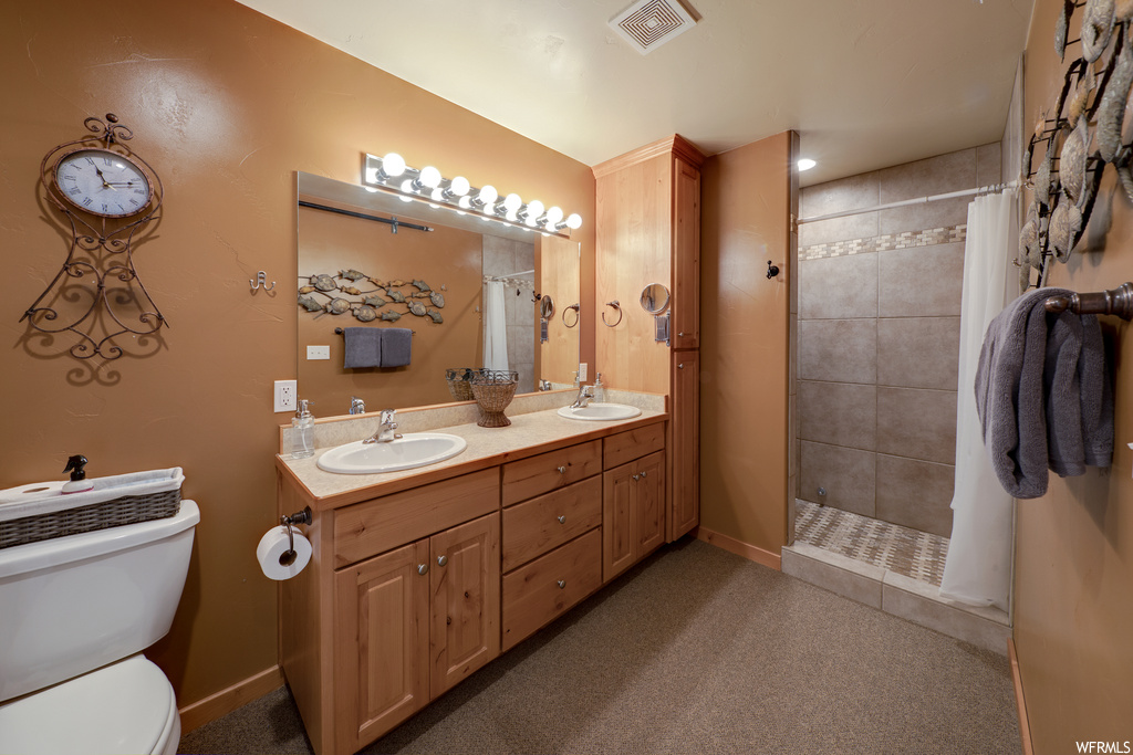 Bathroom with toilet, vanity with extensive cabinet space, walk in shower, and dual sinks