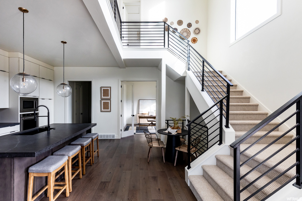 Interior space featuring sink, appliances with stainless steel finishes, a kitchen bar, a towering ceiling, and dark hardwood / wood-style floors