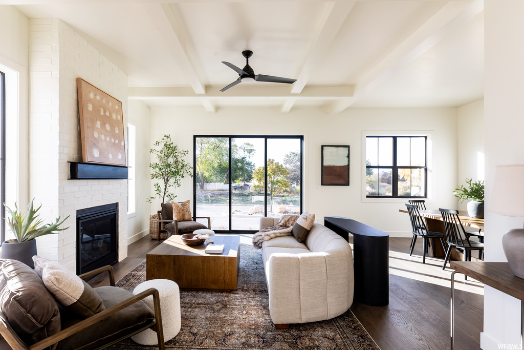 Living room featuring a fireplace, ceiling fan, dark hardwood / wood-style floors, brick wall, and beam ceiling