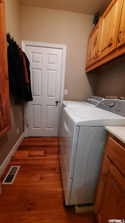 Washroom featuring dark hardwood / wood-style floors, washer and dryer, and cabinets