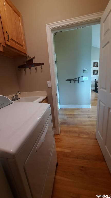 Clothes washing area with cabinets, sink, and light hardwood / wood-style floors