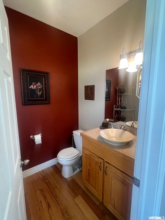 Bathroom with toilet, vanity with extensive cabinet space, and hardwood / wood-style floors