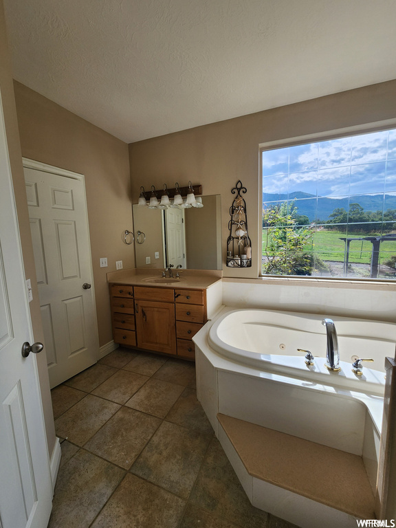 Bathroom featuring a textured ceiling, a bath, tile flooring, a mountain view, and vanity