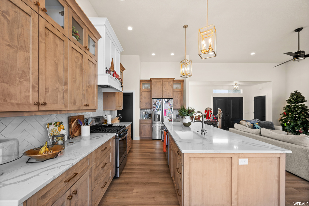 Kitchen with sink, appliances with stainless steel finishes, ceiling fan with notable chandelier, backsplash, and a center island with sink