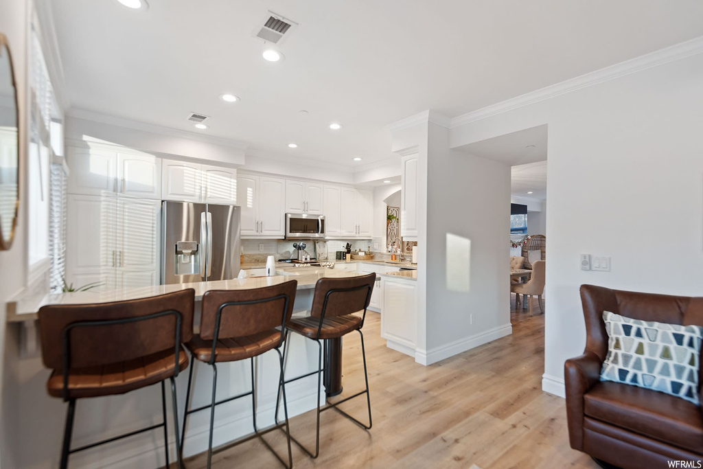 Kitchen featuring light hardwood / wood-style floors, appliances with stainless steel finishes, a breakfast bar area, white cabinets, and backsplash