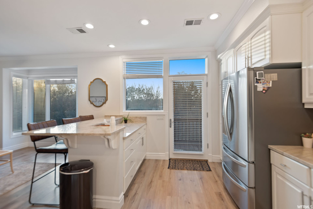 Kitchen featuring ornamental molding, light wood-type flooring, stainless steel refrigerator, and white cabinets