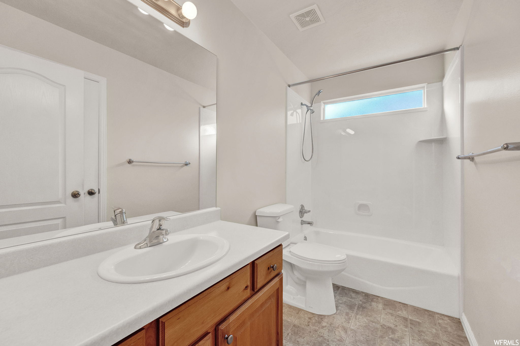 Full bathroom with toilet, tile flooring, large vanity, and washtub / shower combination