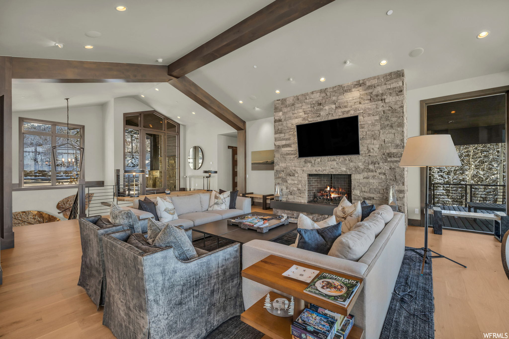 Living room featuring light wood-type flooring, a stone fireplace, and vaulted ceiling