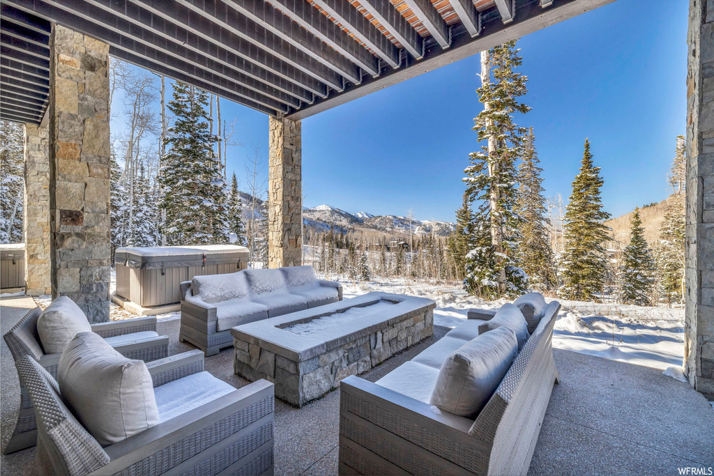 Snow covered patio featuring an outdoor living space with a fire pit, a hot tub, and a mountain view