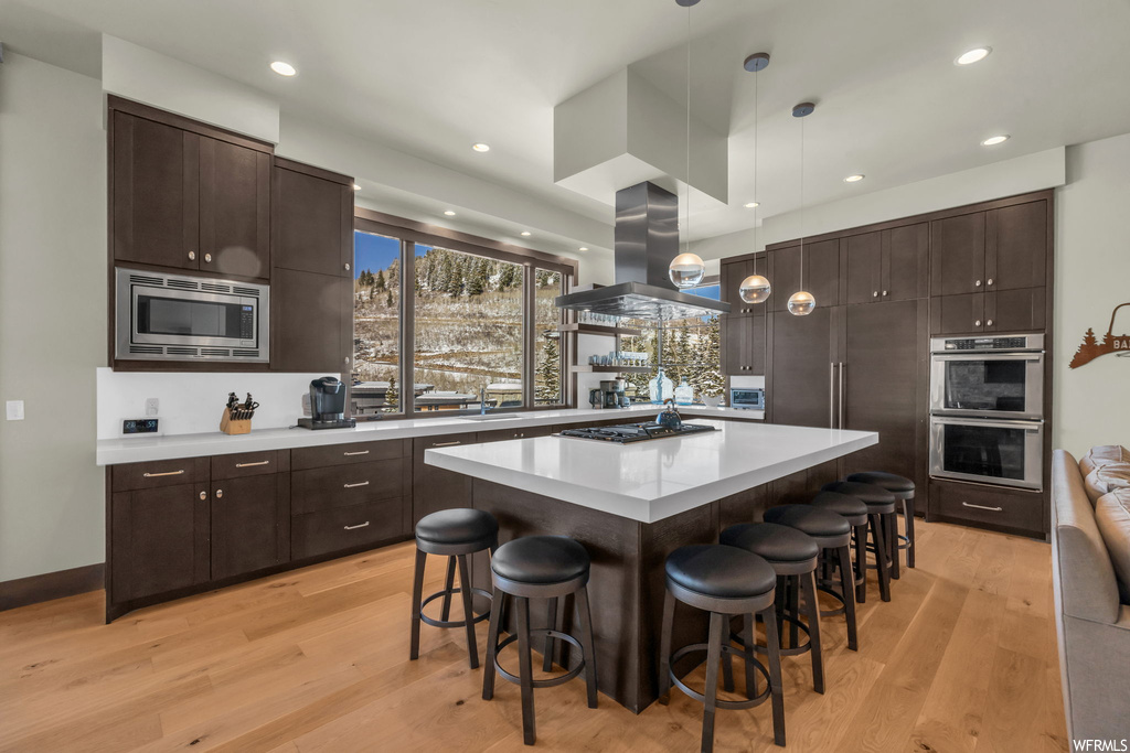 Kitchen with light hardwood / wood-style flooring, stainless steel appliances, a kitchen island, and island exhaust hood