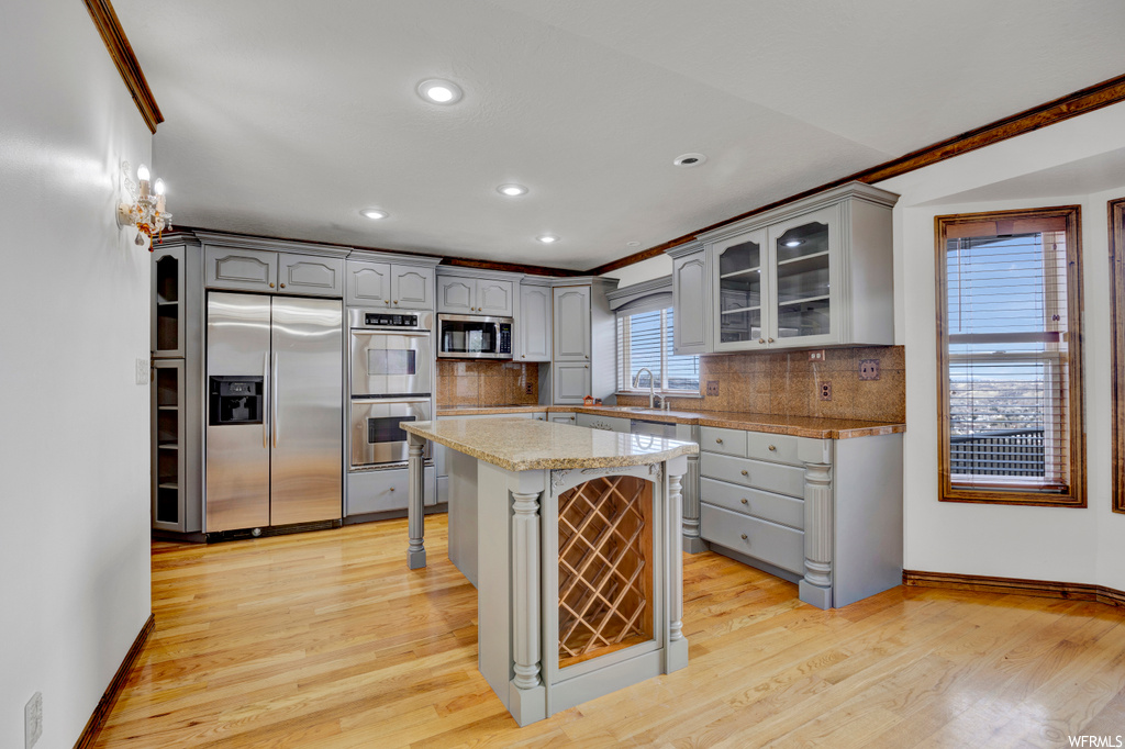Kitchen with gray cabinetry, appliances with stainless steel finishes, light hardwood / wood-style floors, tasteful backsplash, and a kitchen island