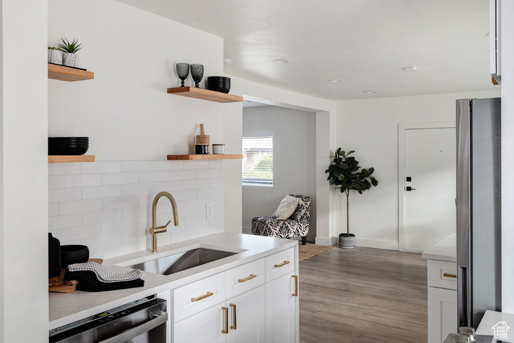 Kitchen featuring stainless steel appliances, tasteful backsplash, light hardwood / wood-style flooring, white cabinets, and sink