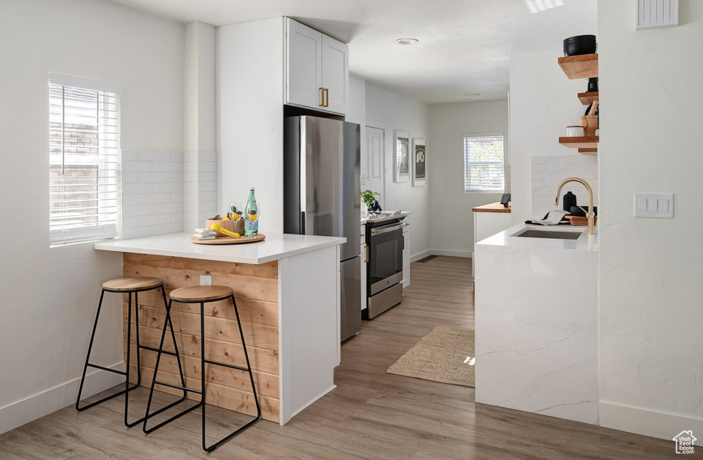 Kitchen featuring white cabinets, appliances with stainless steel finishes, light wood-type flooring, and a kitchen breakfast bar