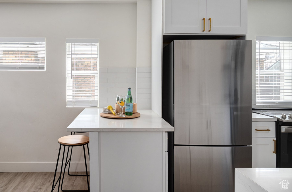 Kitchen featuring stainless steel fridge, white cabinets, light hardwood / wood-style floors, and a kitchen breakfast bar