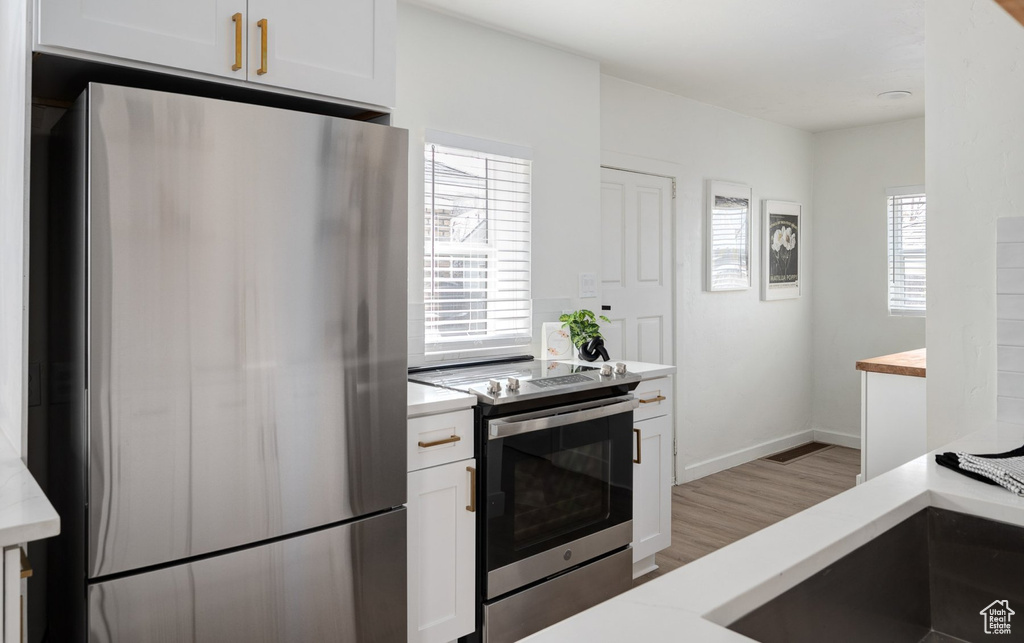 Kitchen with sink, white cabinets, appliances with stainless steel finishes, and light hardwood / wood-style flooring