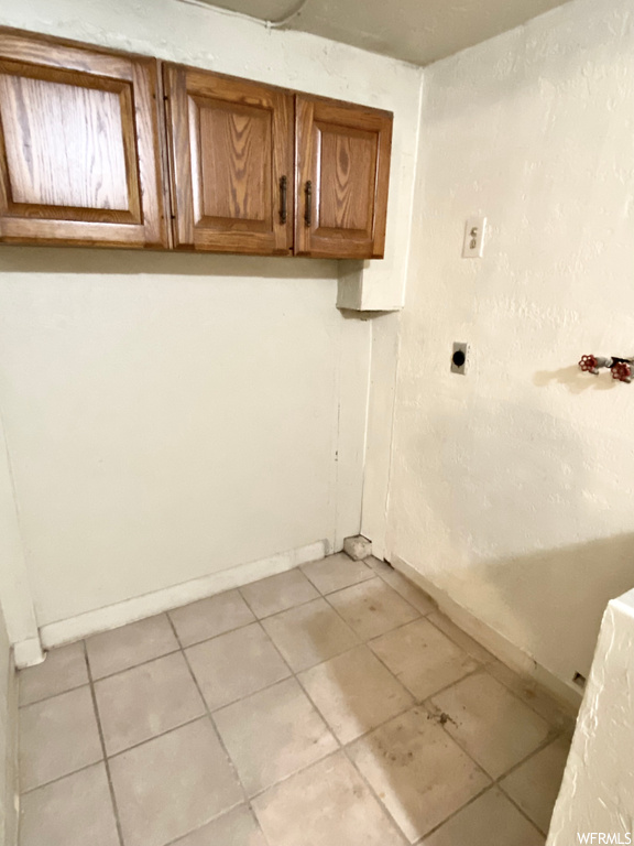 Washroom with electric dryer hookup, cabinets, and light tile flooring