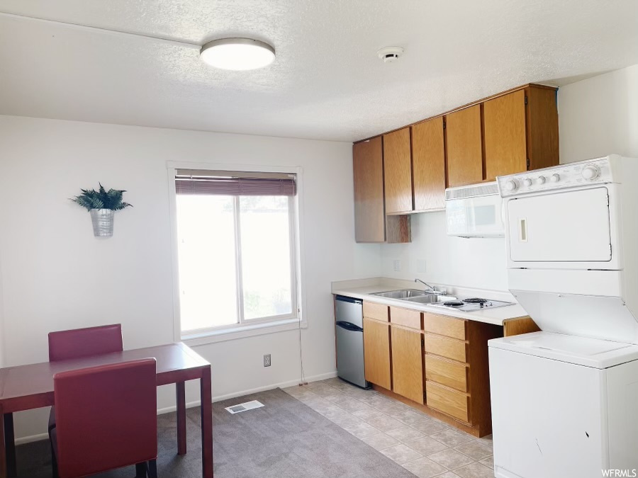 Kitchen with sink, stainless steel dishwasher, light tile flooring, and stacked washer and clothes dryer