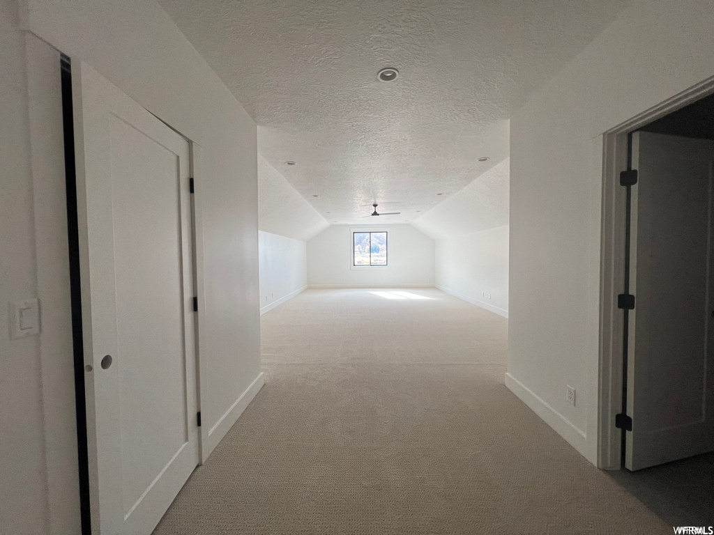 Corridor featuring lofted ceiling, light colored carpet, and a textured ceiling