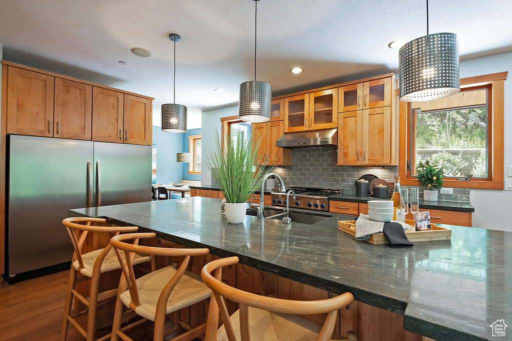 Kitchen with an island with sink, high end fridge, wood-type flooring, pendant lighting, and tasteful backsplash