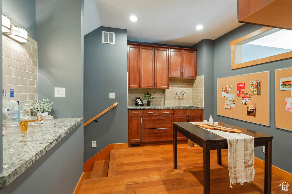 Kitchen with light hardwood / wood-style floors, sink, backsplash, and light stone counters