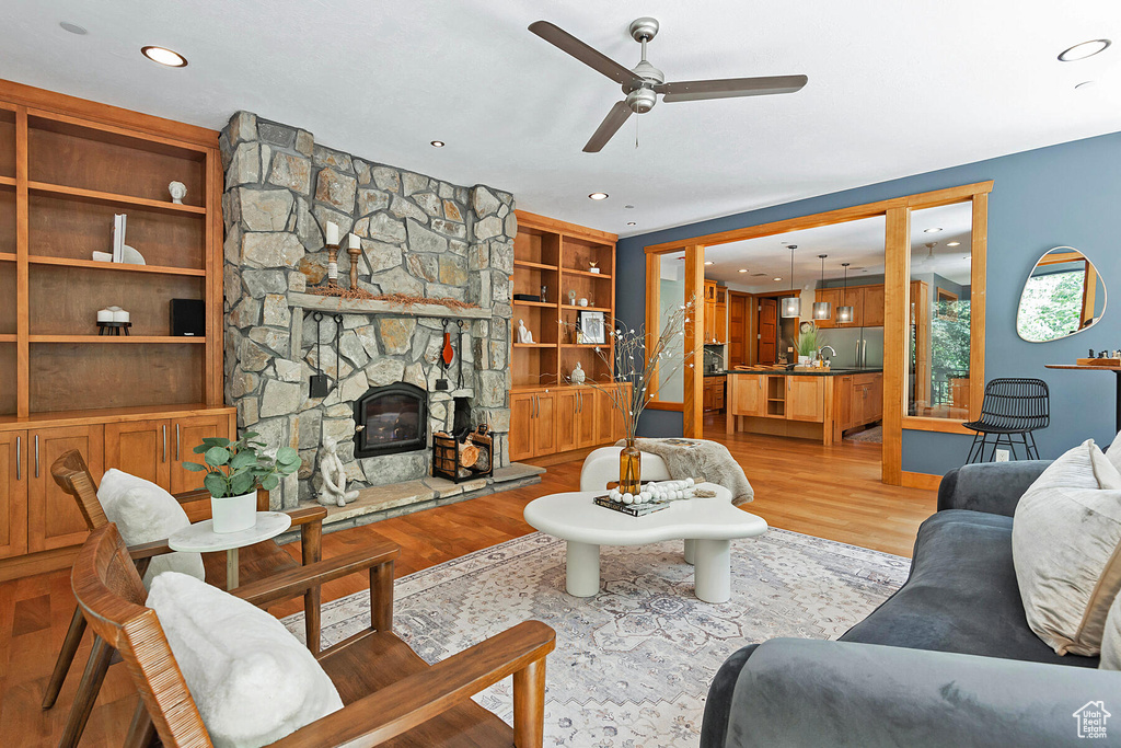 Living room with ceiling fan, a stone fireplace, light hardwood / wood-style floors, and built in shelves