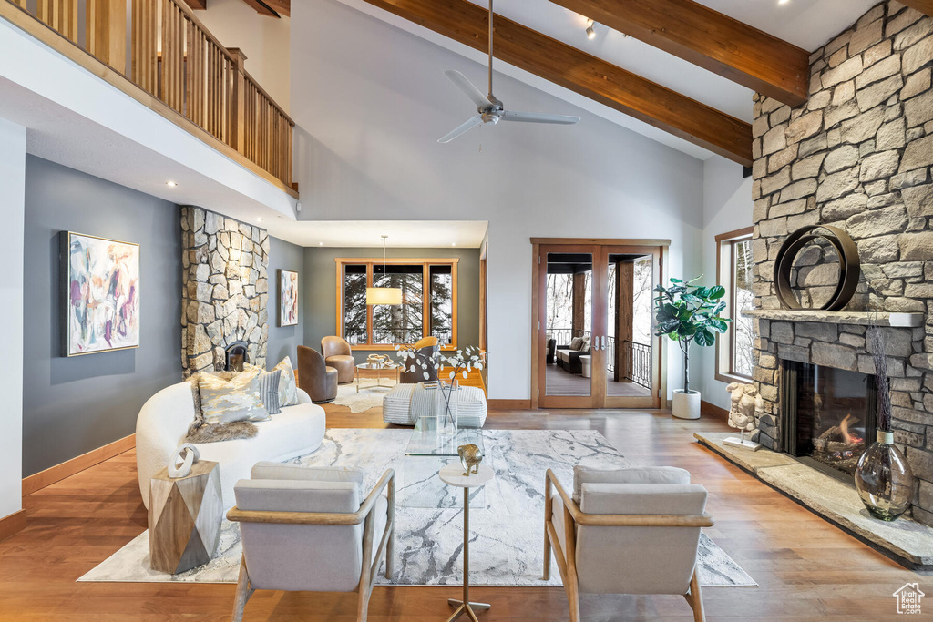 Living room featuring ceiling fan, hardwood / wood-style flooring, a stone fireplace, high vaulted ceiling, and beamed ceiling