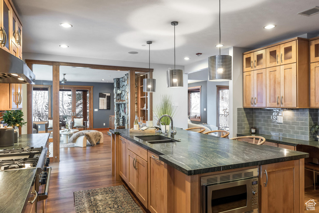 Kitchen with backsplash, stainless steel microwave, an island with sink, dark wood-type flooring, and sink