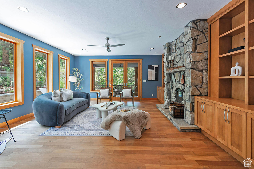 Living room with a stone fireplace, light hardwood / wood-style floors, french doors, and ceiling fan