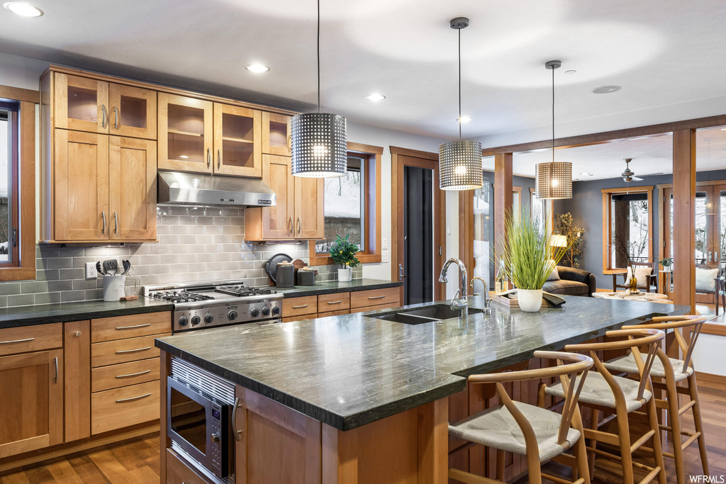 Kitchen with stainless steel microwave, hanging light fixtures, sink, a kitchen island with sink, and dark hardwood / wood-style floors