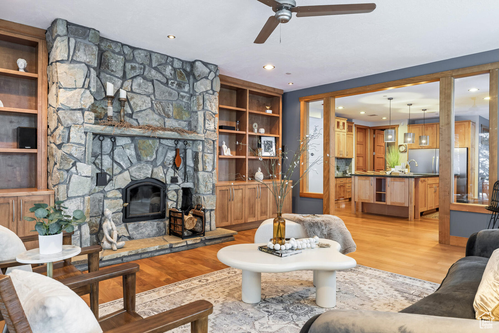 Living room with ceiling fan, light hardwood / wood-style flooring, a fireplace, built in features, and sink