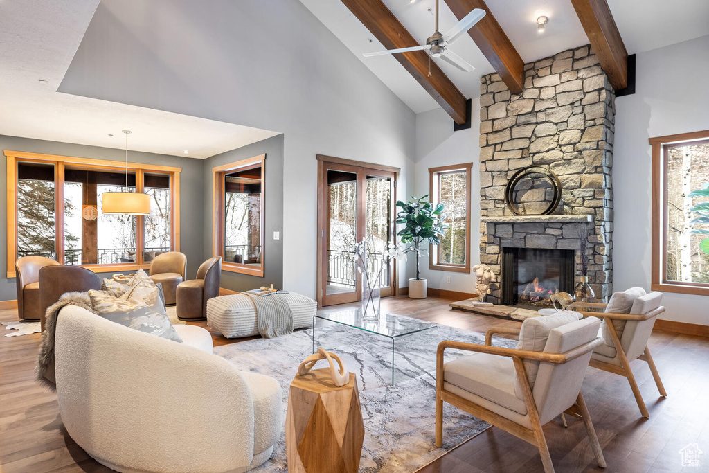 Living room featuring a stone fireplace, ceiling fan, hardwood / wood-style floors, beam ceiling, and high vaulted ceiling