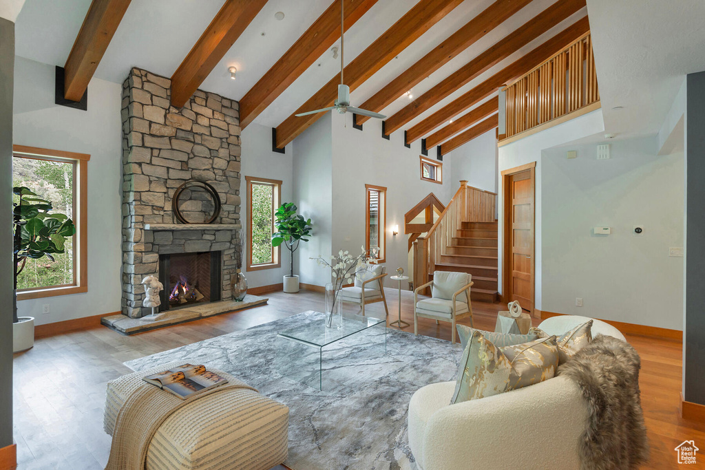 Living room with a fireplace, beamed ceiling, hardwood / wood-style floors, high vaulted ceiling, and ceiling fan