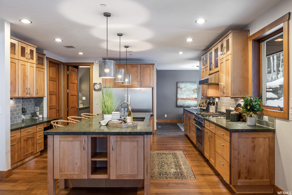 Kitchen with dark wood-type flooring, a center island with sink, high end appliances, and backsplash