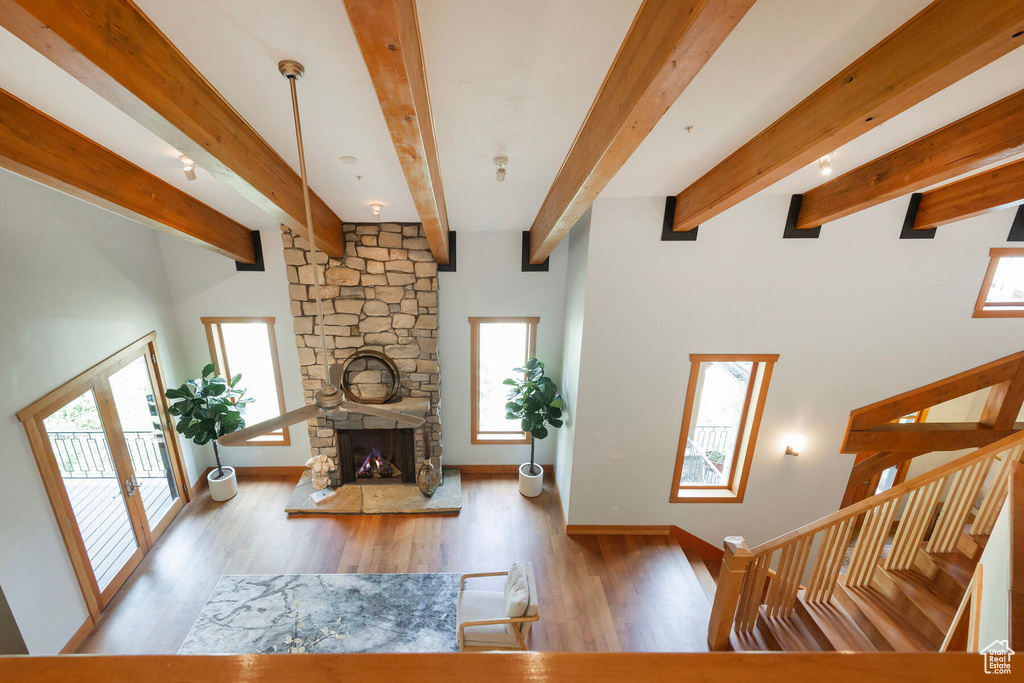 Living room with beam ceiling, a stone fireplace, and hardwood / wood-style floors