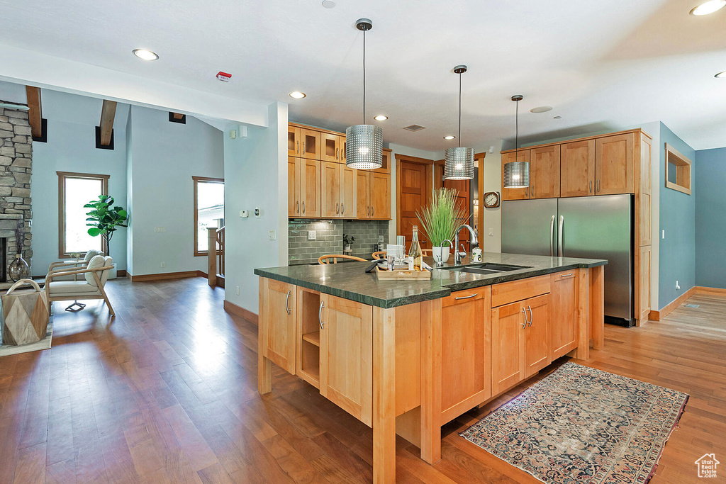 Kitchen featuring backsplash, a stone fireplace, wood-type flooring, sink, and pendant lighting