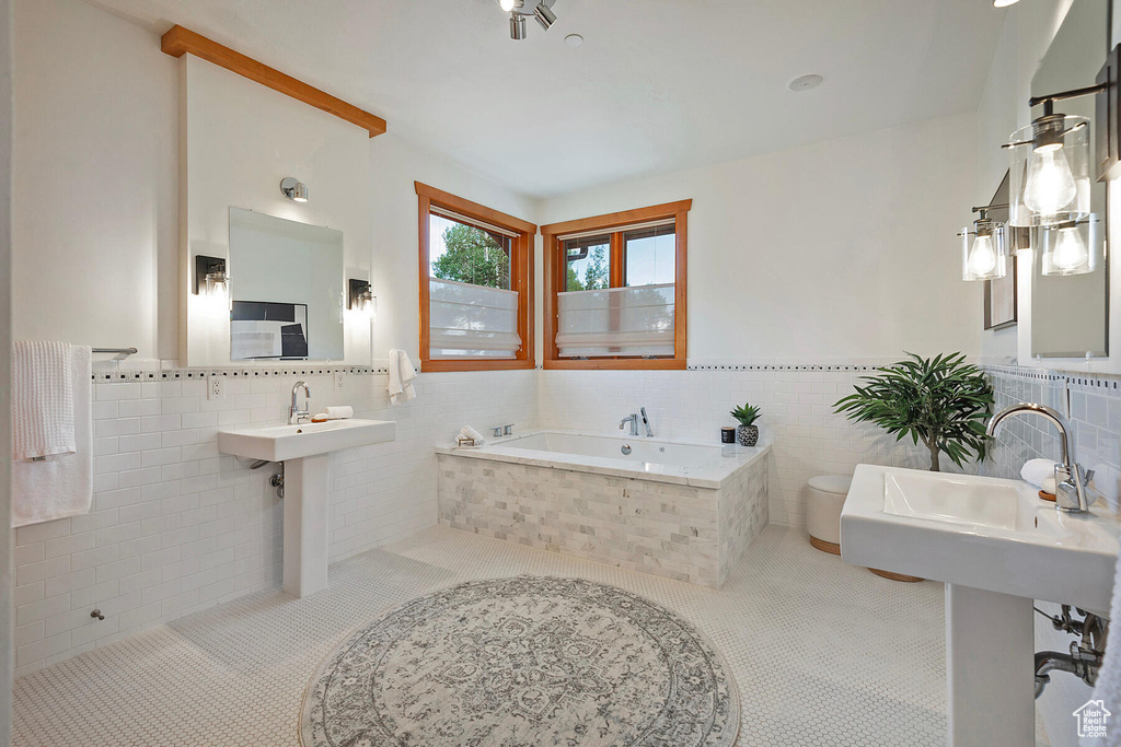 Bathroom with tiled bath, backsplash, sink, and tile walls