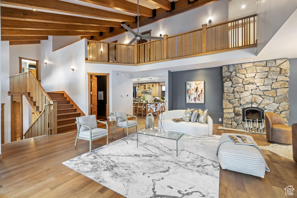 Living room featuring beamed ceiling, wood-type flooring, a stone fireplace, high vaulted ceiling, and ceiling fan