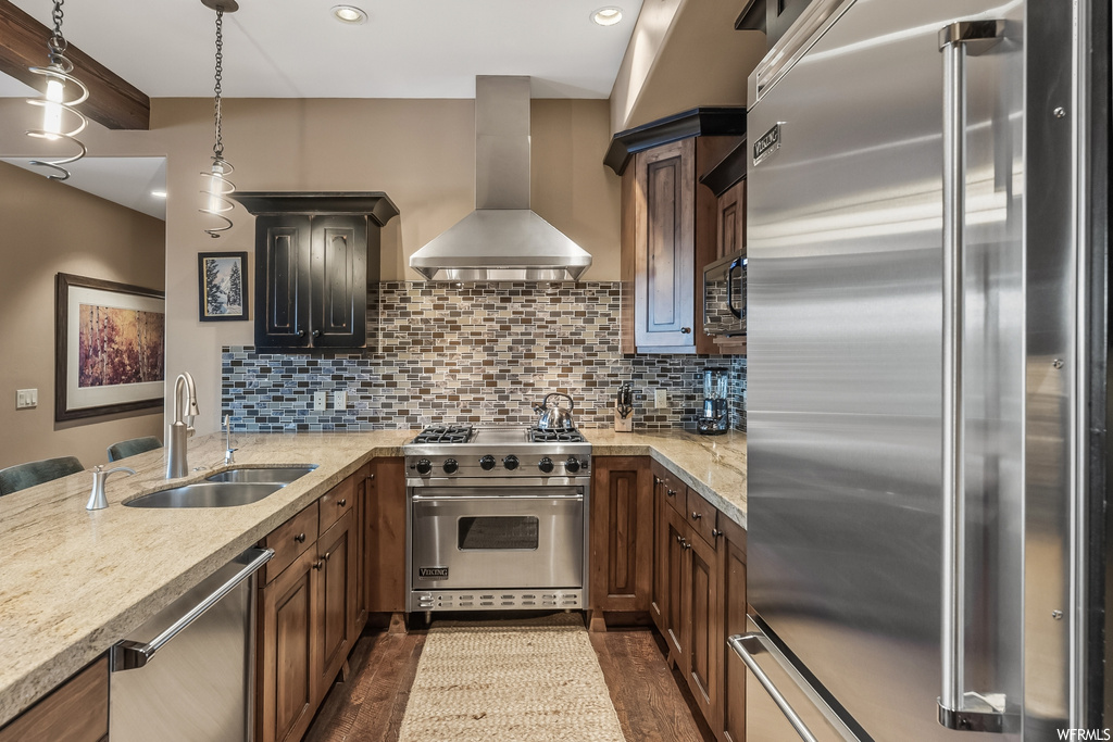 Kitchen featuring sink, built in appliances, decorative light fixtures, dark hardwood / wood-style floors, and range hood
