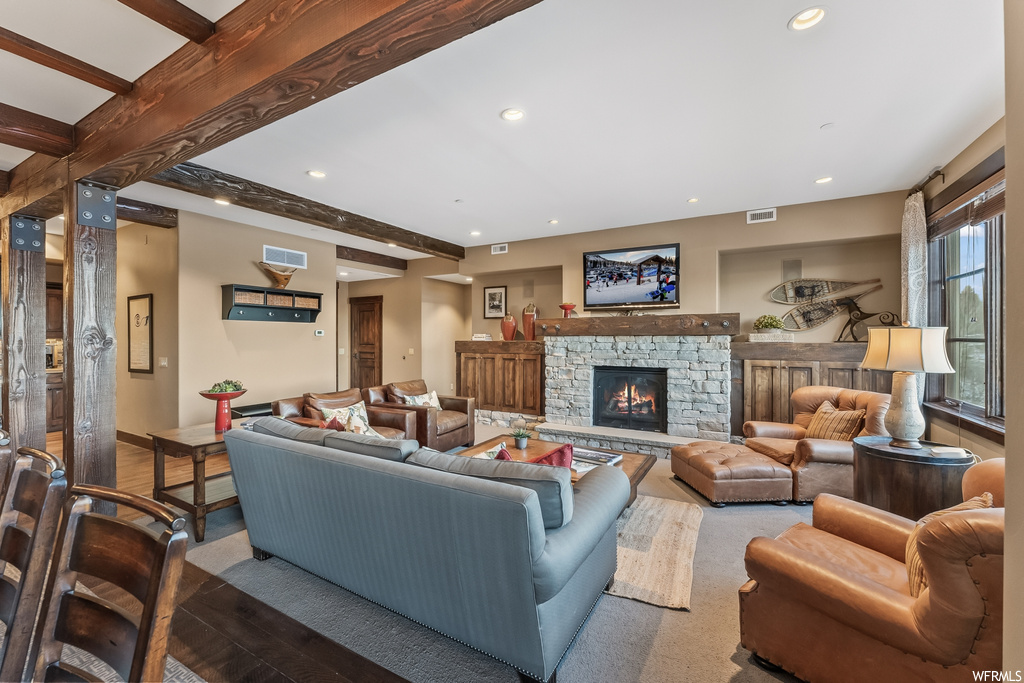 Living room featuring beamed ceiling, a stone fireplace, and hardwood / wood-style flooring