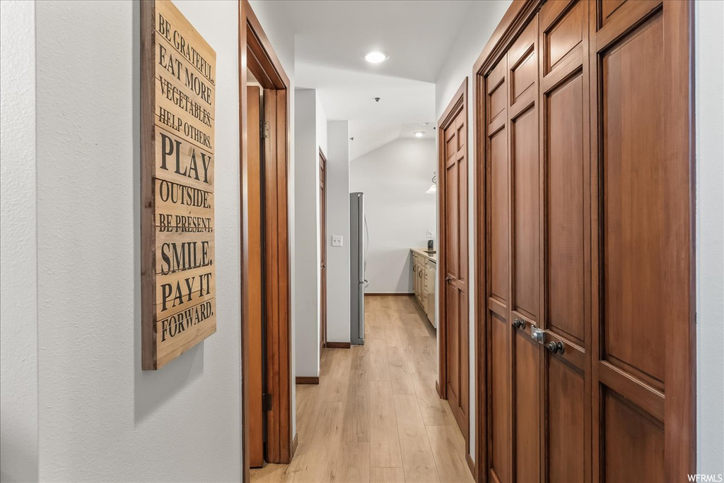 Corridor with light hardwood / wood-style flooring and lofted ceiling