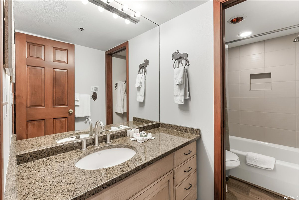 Full bathroom featuring tiled shower / bath combo, toilet, vanity with extensive cabinet space, and hardwood / wood-style flooring