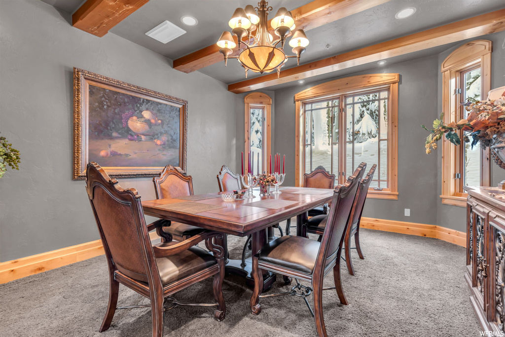 Dining area with a notable chandelier, a wealth of natural light, carpet flooring, and beamed ceiling