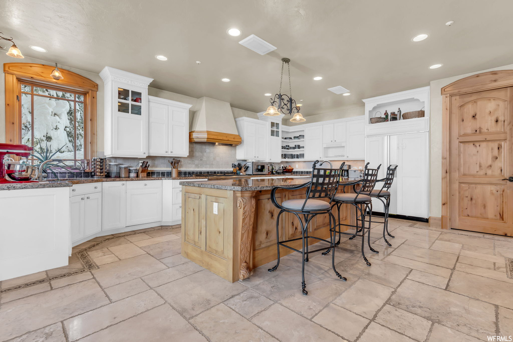 Kitchen with custom exhaust hood, a center island, light tile flooring, and white cabinetry