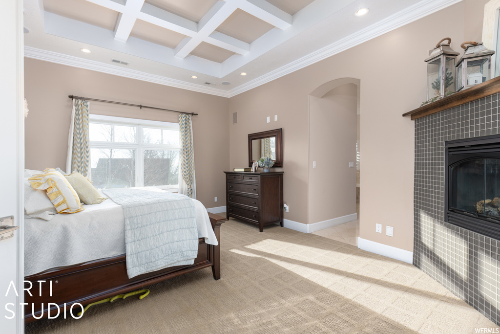 Bedroom with coffered ceiling, light colored carpet, ornamental molding, a tile fireplace, and beam ceiling